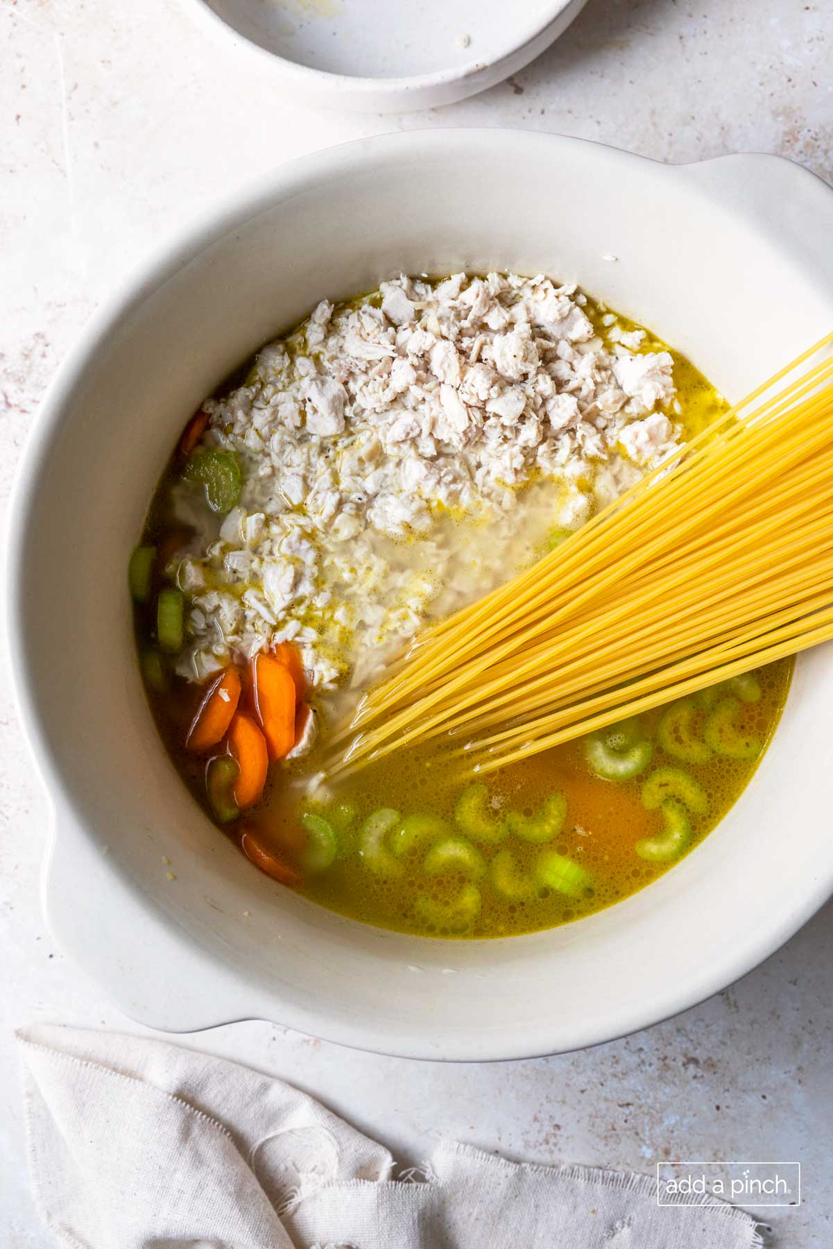 Photograph of chicken noodle soup ingredients added to a Dutch oven. 