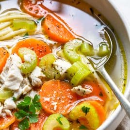 Photo of a bowl of chicken noodle soup in a white bowl with a spoon.