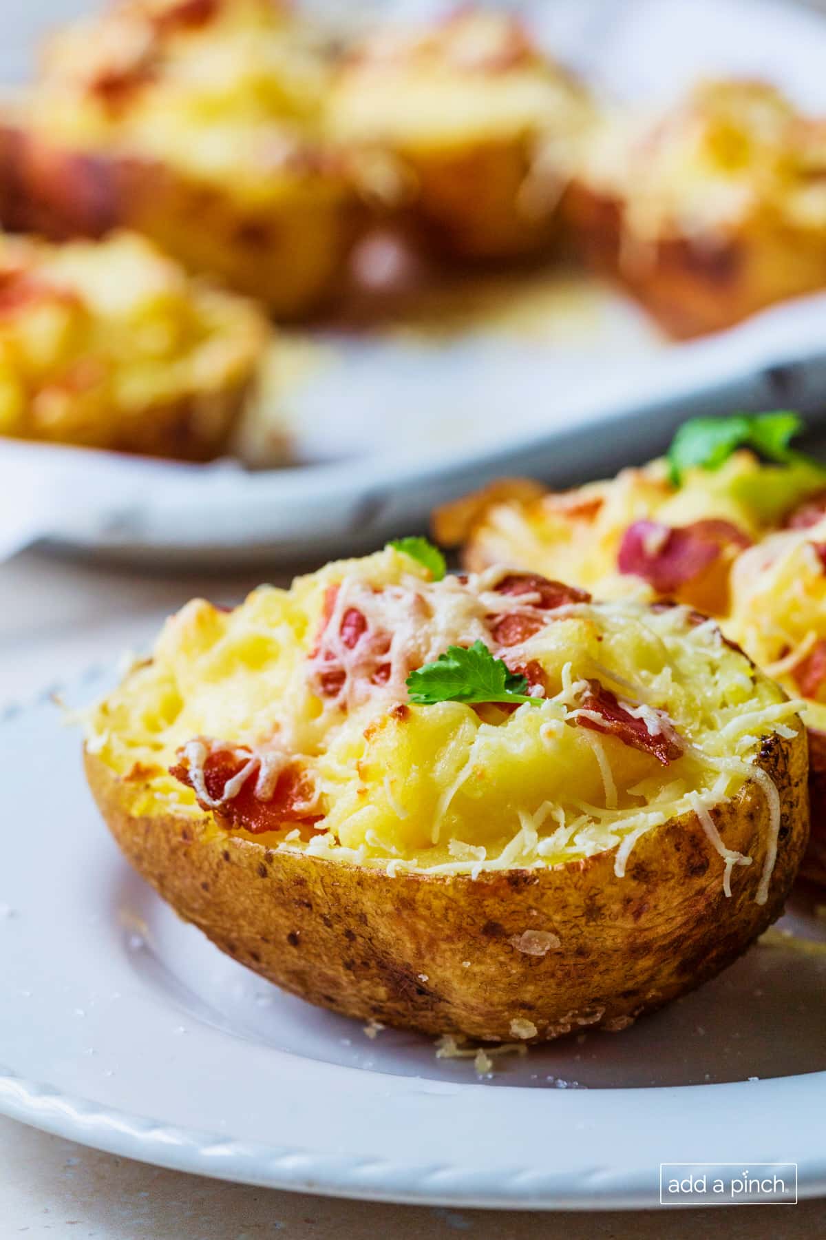 Photo of twice baked potatoes on a white plate with platter of more potatoes in the background.