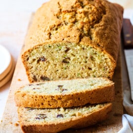 Loaf of zucchini bread with slices cut for serving on a wooden surface.