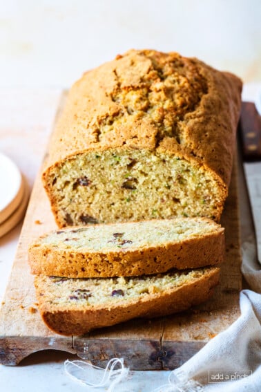 Loaf of zucchini bread with slices cut for serving on a wooden surface.