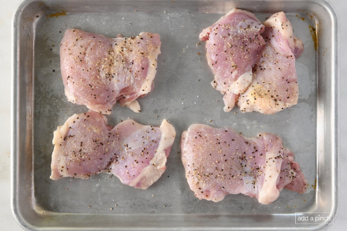 Marinated chicken thighs on a baking sheet.