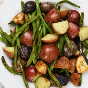 Photo of green beans and potatoes in a white bowl on a marble surface.