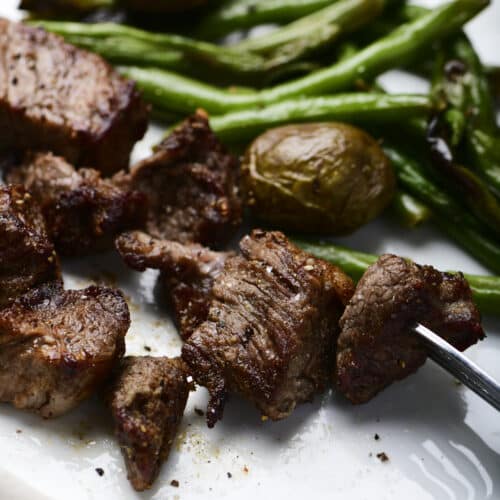 Photo of steak bites served with green beans and potatoes on a white plate.