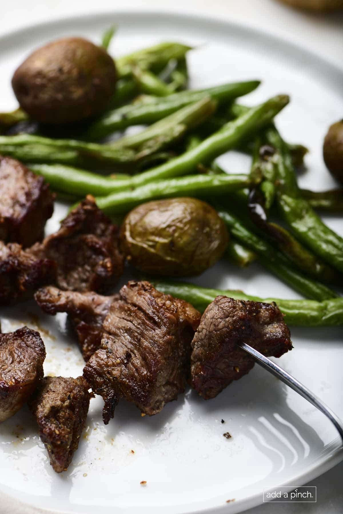 Photo of steak, potatoes, and green beans on a white plate.