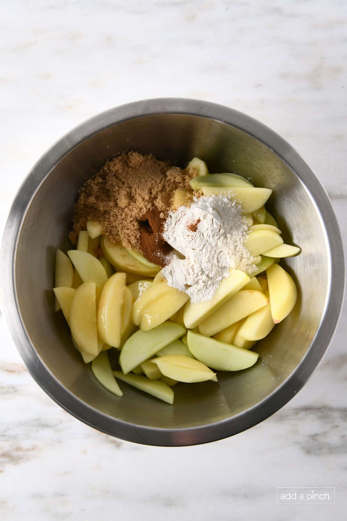 Stainless mixing bowl with apples, cinnamon, brown sugar flour and other ingredients to make apple crisp filling.