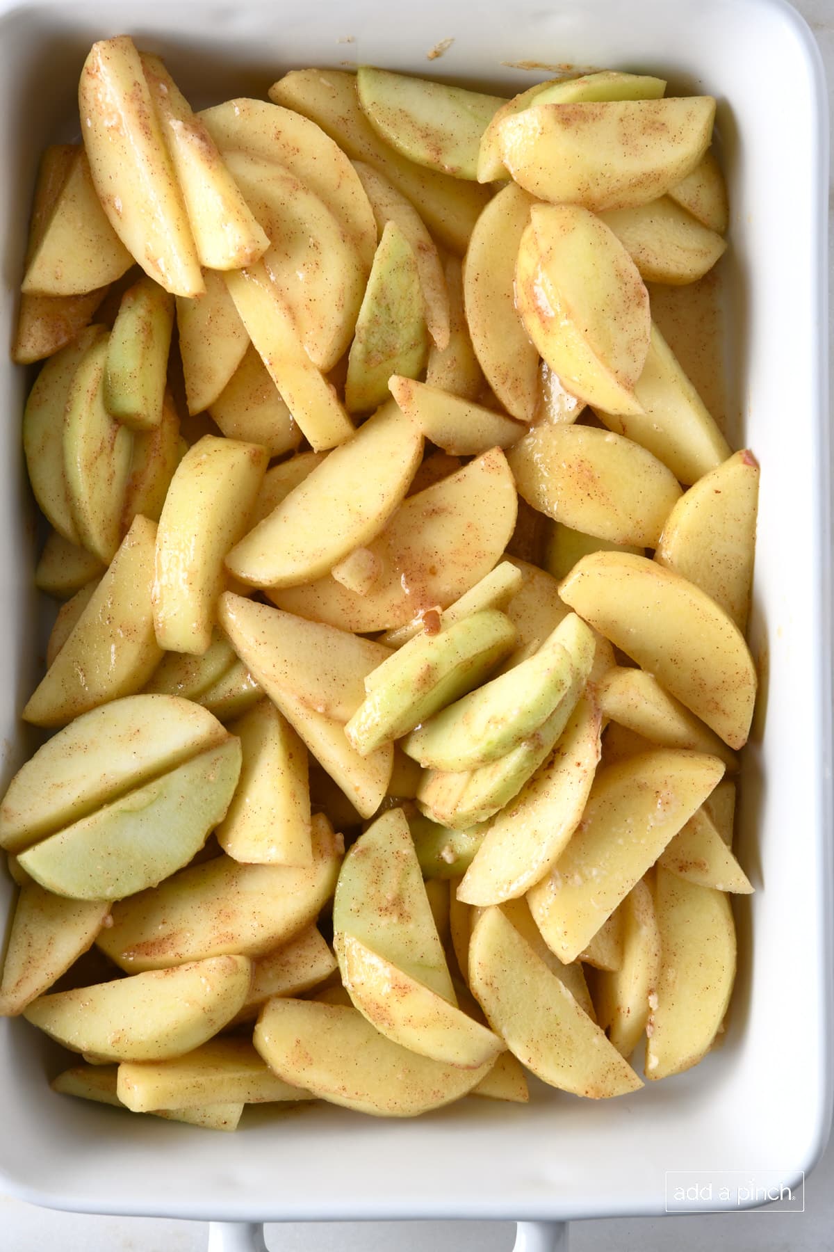 Baking dish with sliced apples mixed with other ingredients to make the apple crisp filling. 