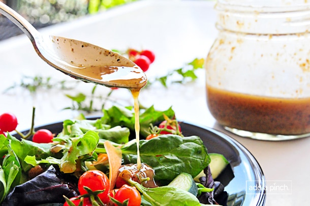 Image of buttermilk dressing being spooned onto a plate of green salad with tomatoes, cheese, and avocado.