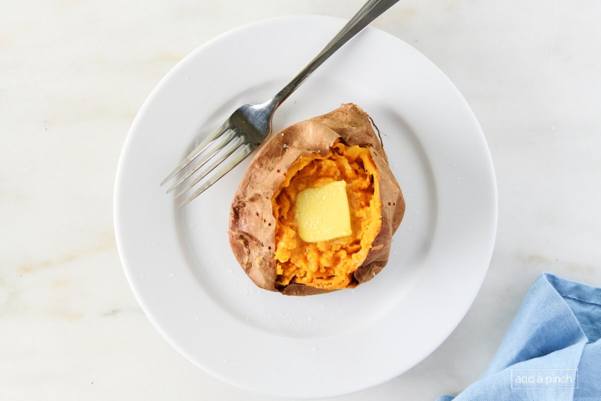 Sweet potato on a white plate served with a pat of butter and salt.