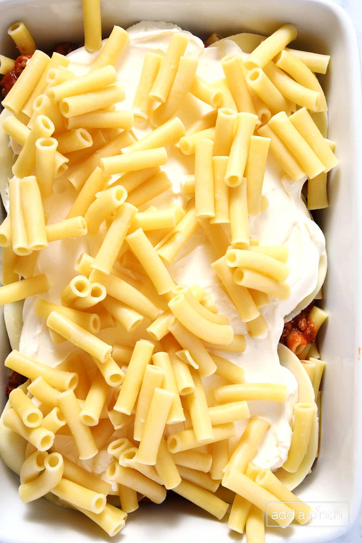 White baking dish filled with noodles, meat sauce, cheese and more noodles.