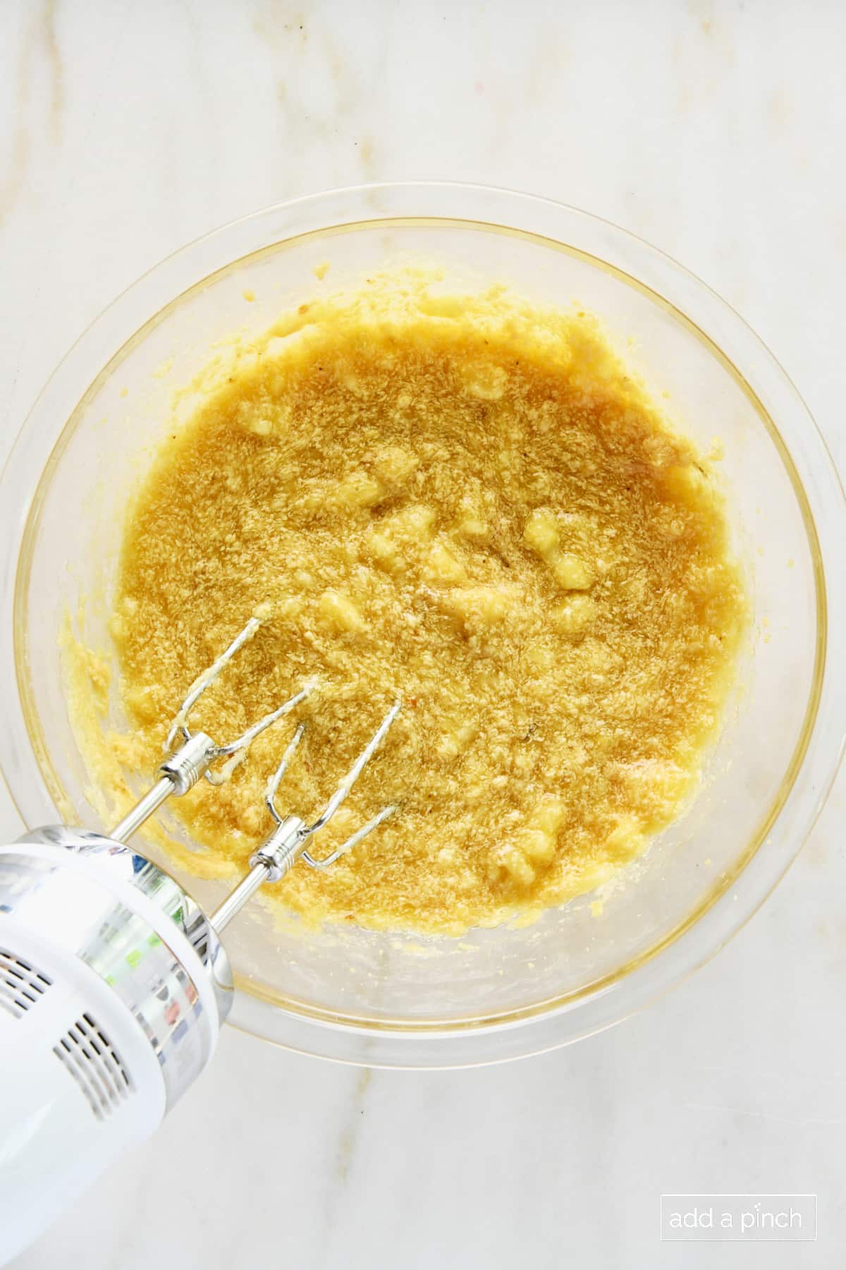 Bananas, brown sugar, and butter mixed together in a glass bowl with a hand mixer.