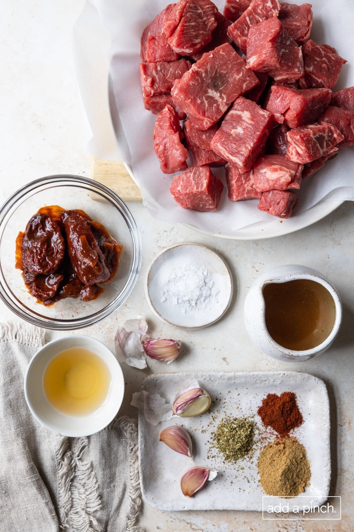 Photograph of recipe ingredients - beef, salt, garlic, apple cider vinegar, adobo, beef broth, and seasonings - for beef barbacoa.
