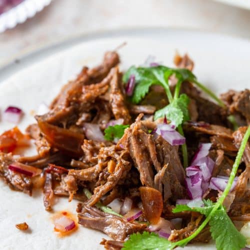 Photo of barbacoa on soft tortilla with cilantro, red onion, and extra sauce drizzled on top.