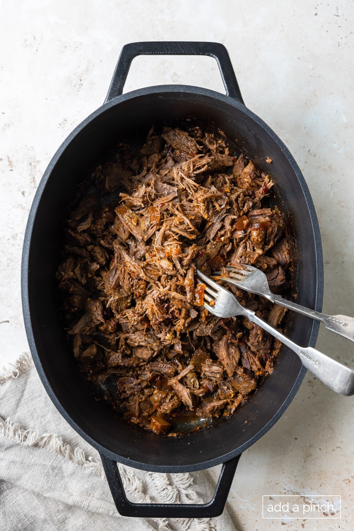 Photograph of barbacoa beef shredded in a pot with two forks.
