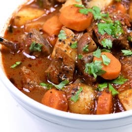 Photograph of homemade beef stew in a white bowl on a white background. // addapinch.com