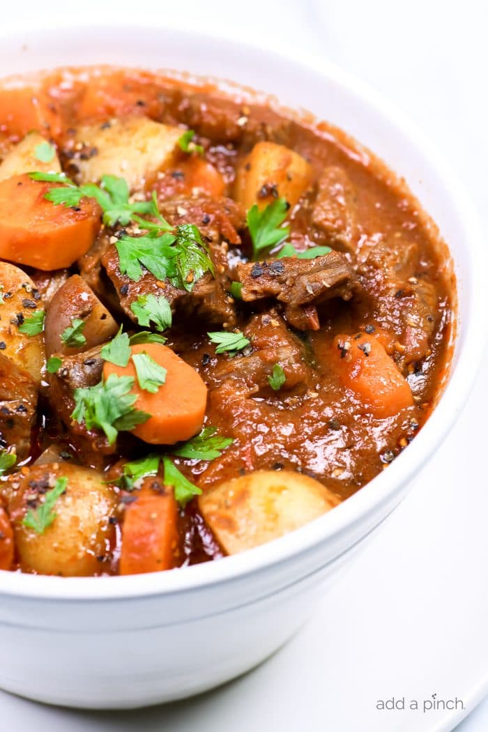 Closeup photograph of beef stew in a white bowl on a white counter. // addapinch.com