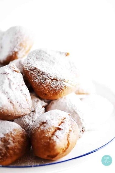 Beignets dusted with powdered sugar served on white plate.