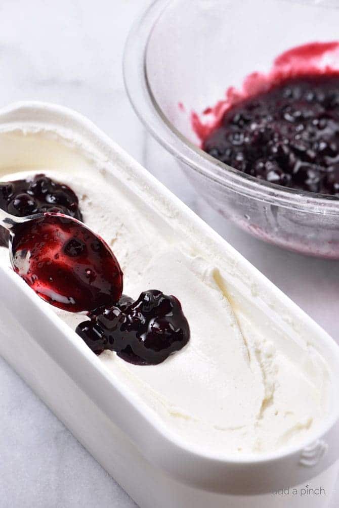 Spooning blueberry sauce into tub of ice cream, beside bowl of blueberry sauce // addapinch.com