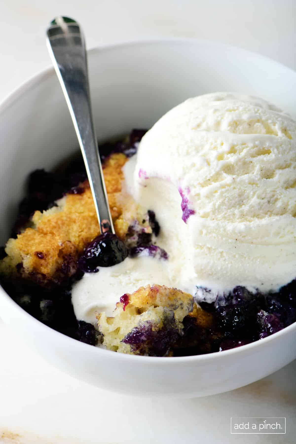 Blueberry cobbler with vanilla ice cream in a white bowl with a spoon.