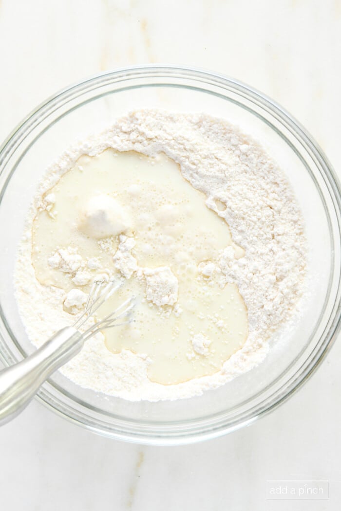 Milk added to dry ingredients in a glass bowl with a whisk