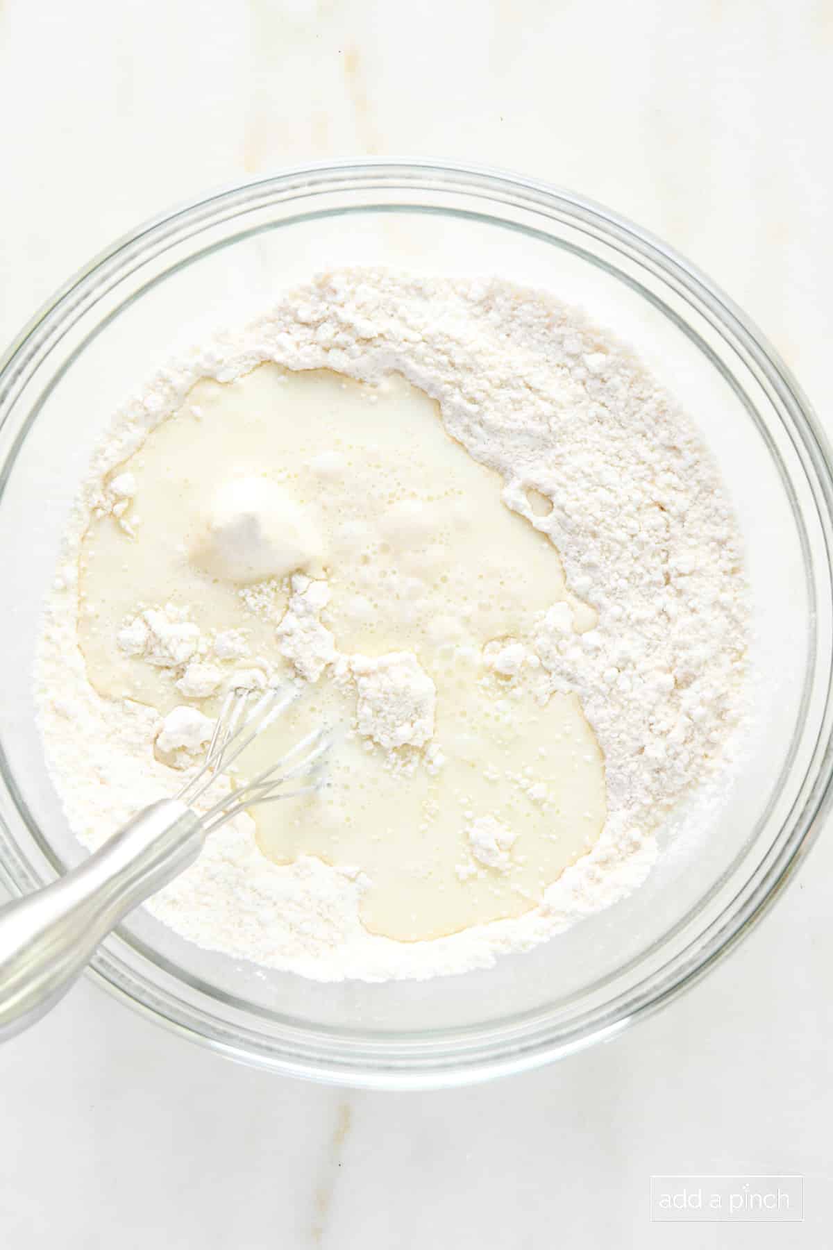 Milk added to dry ingredients in a glass bowl with a whisk