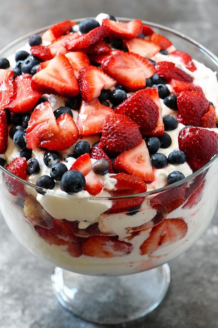 Layers of blueberries, strawberries, cake, whipped cream and pudding alternate in a glass trifle bowl.