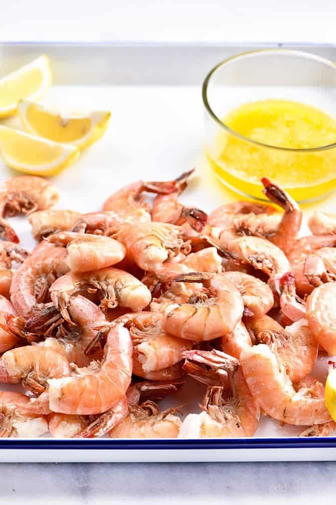 Boiled Shrimp piled on a white platter, along with lemon wedges and drawn butter.