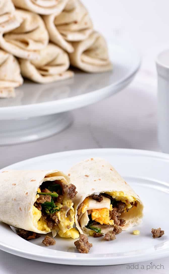 Breakfast burrito on a white plate with stack in the background on a white plate.