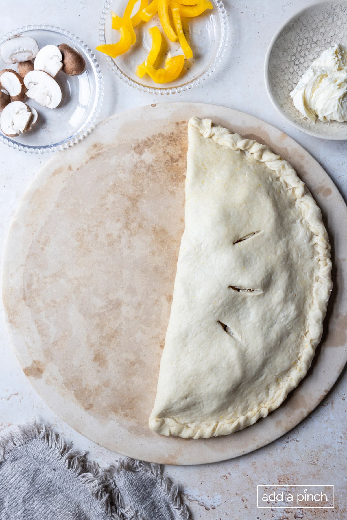 Calzone edges crimped and dough sliced for steam to escape while baking.