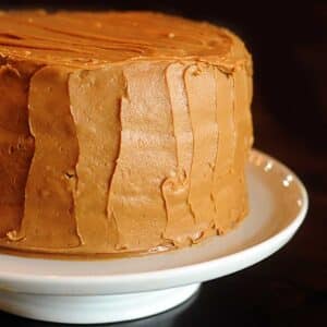 Caramel cake on a white cake stand on a dark wooden table.