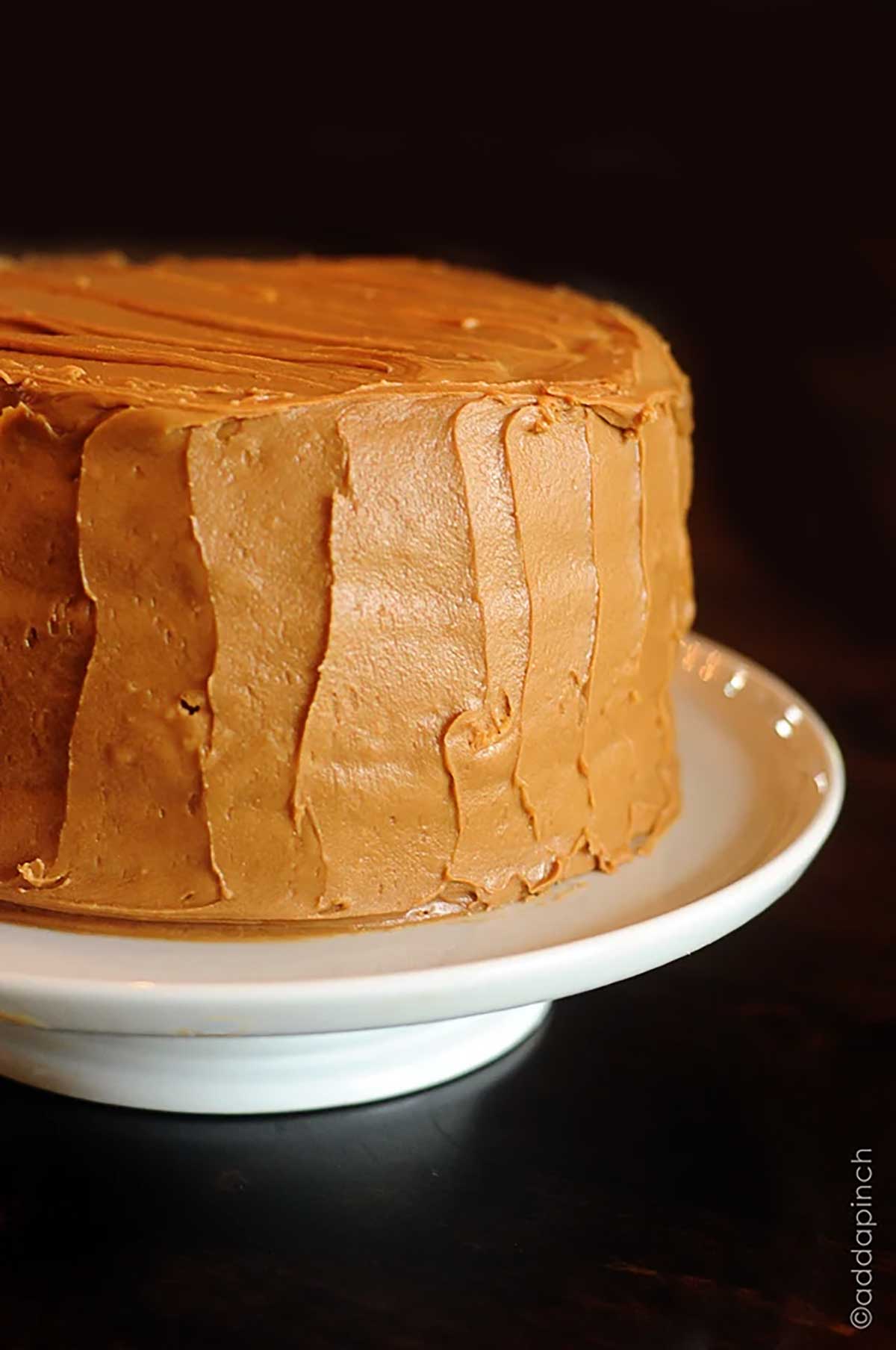 Caramel cake on a white cake stand on a dark wooden table.