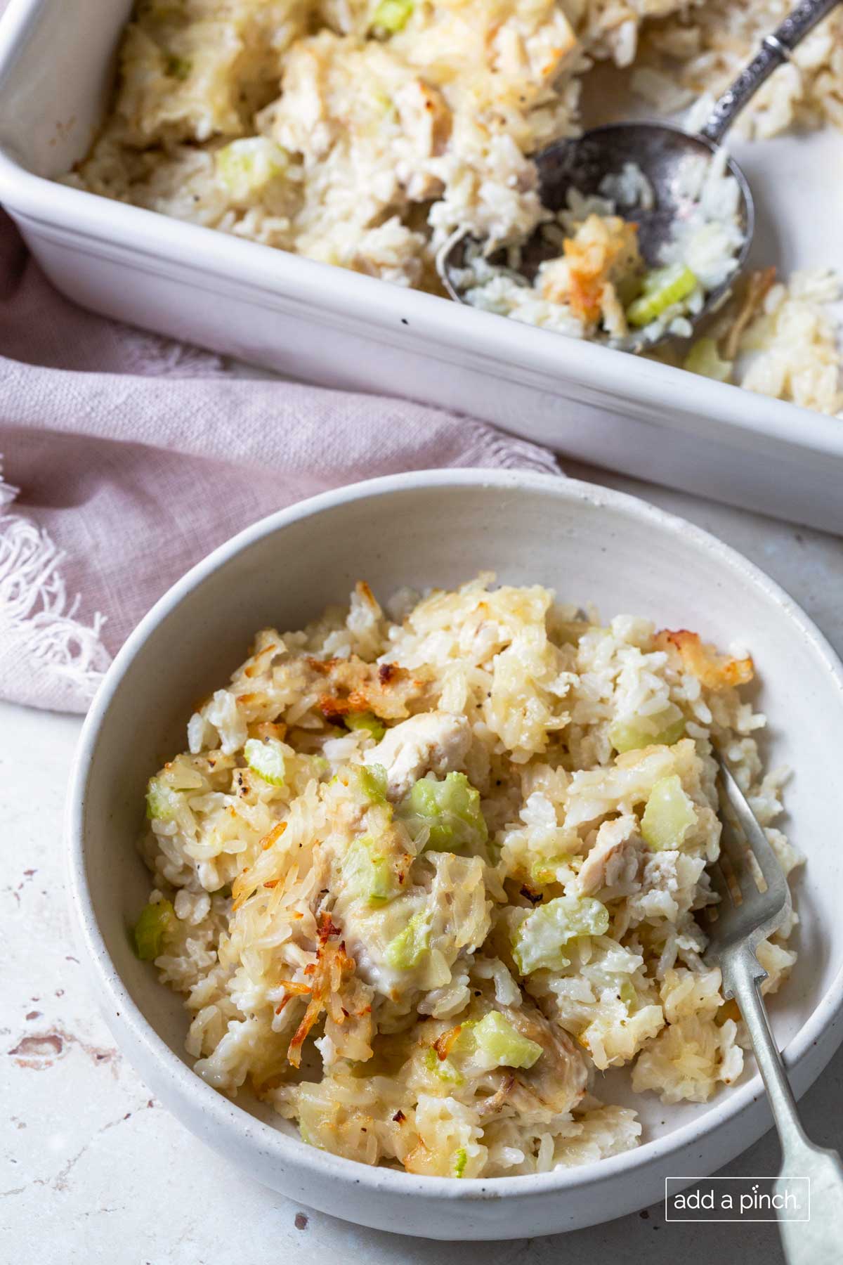 White bowl filled with serving of chicken and rice casserole with a silver fork.