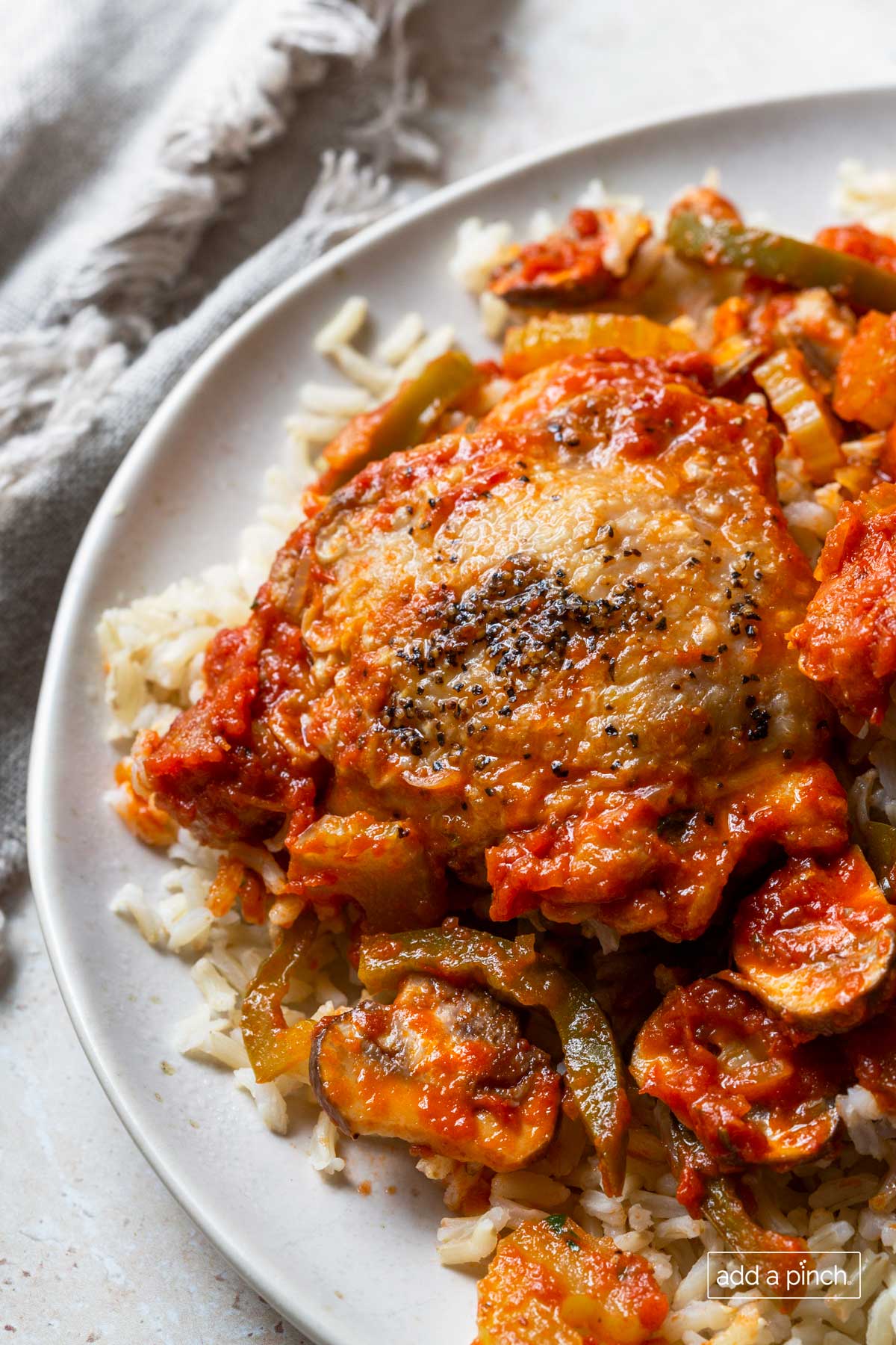 Photo of chicken cacciatore with chicken, peppers, and mushrooms on rice on a white plate.