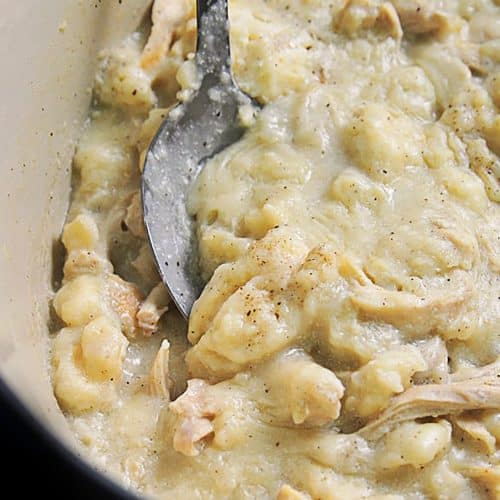 Photo of chicken and dumplings in a Dutch oven with a serving spoon.