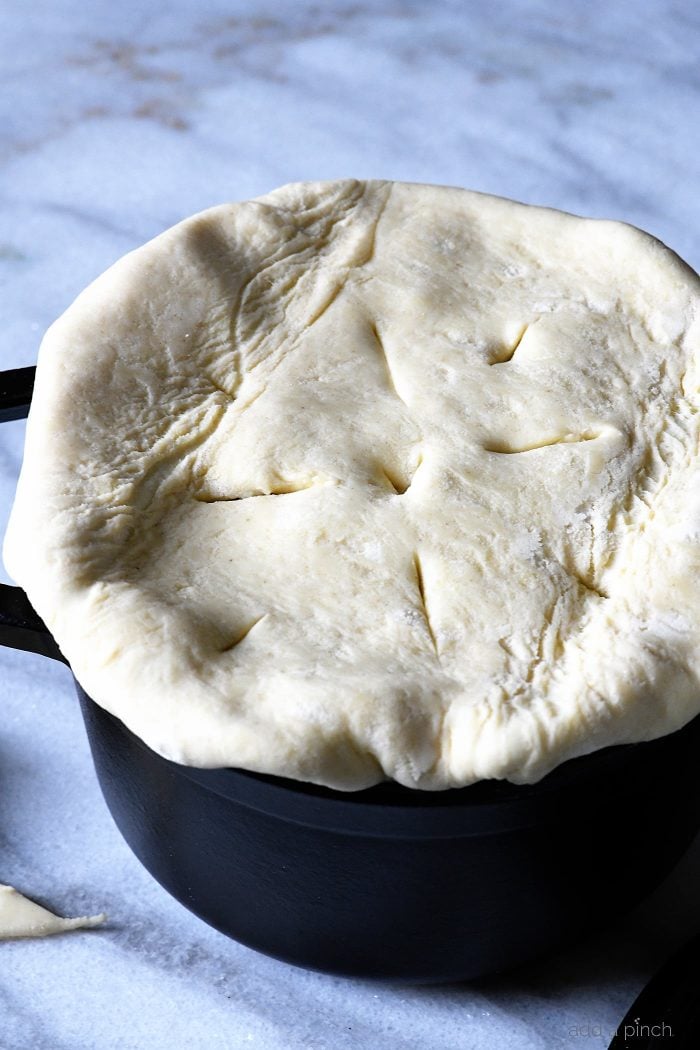 Puff Pastry is laid across top of black dutch oven prior to baking. On marble countertop.