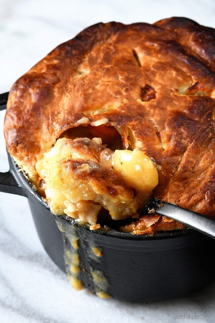 Spoonful of Chicken Pot Pie with puff pastry crust being dipped from dutch oven.