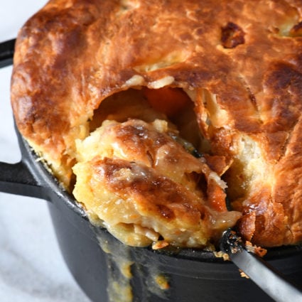 Black dutch oven holds a golden brown crust of a chicken pot pie being spooned out for serving.