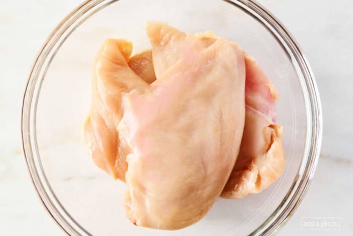 Chicken breast in a glass bowl on a marble countertop.