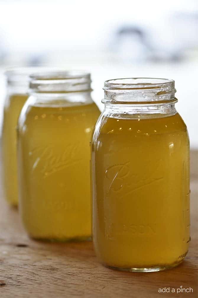 Chicken stock in ball canning jars on a wooden counter.