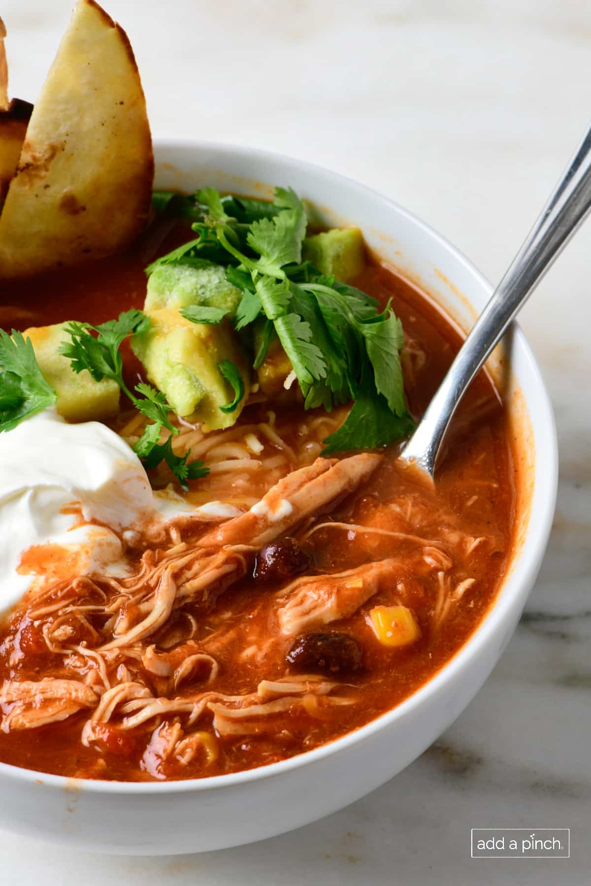 Bowl of chicken tortilla soup garnished with avocados, cilantro, crispy tortilla strips and sour cream. 