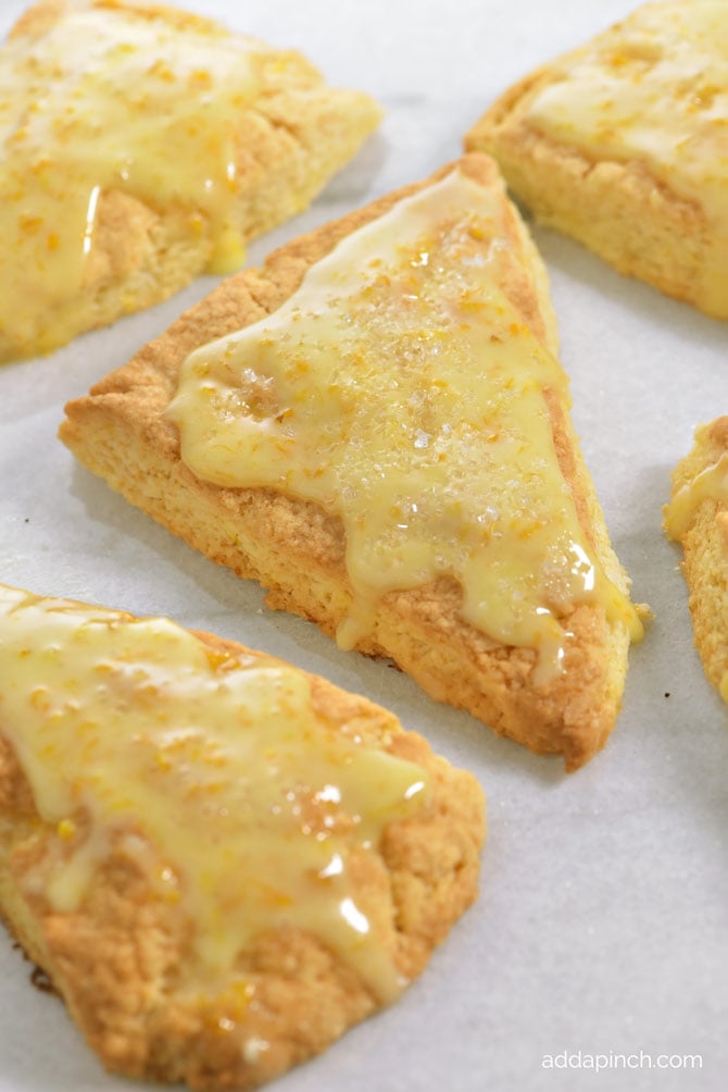 Scones topped with orange glaze on parchment paper - addapinch.com