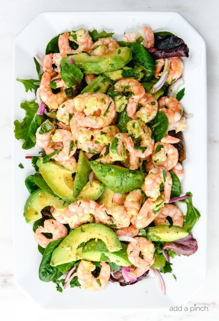 Photograph of citrus shrimp avocado salad on a white platter on white marble. // addapinch.com