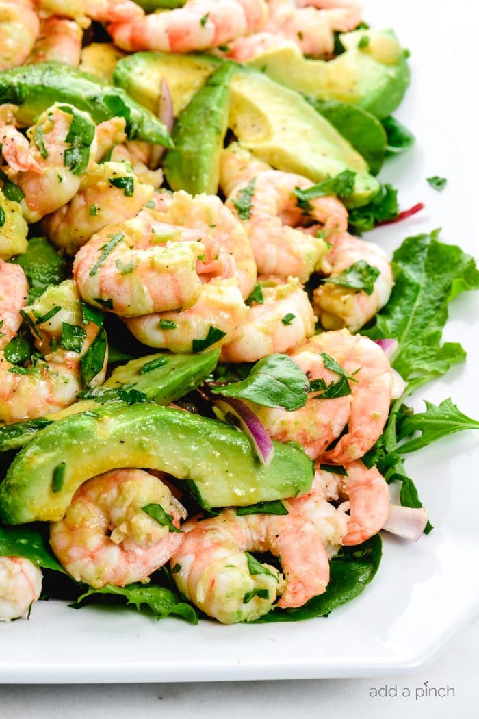 Close up photograph of citrus shrimp avocado salad on a white platter. // addapinch.com