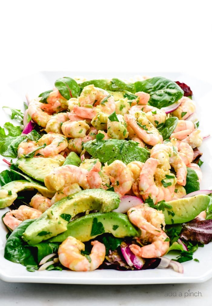 Photograph of white platter filled with citrus shrimp avocado salad with red onions. 