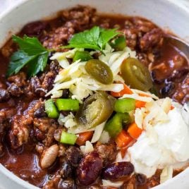 Bowl of the best classic chili made with beef, beans, tomatoes and spices and then topped with your favorite toppings. Photographed in a white bowl with garnish on a white surface.// addapinch.com