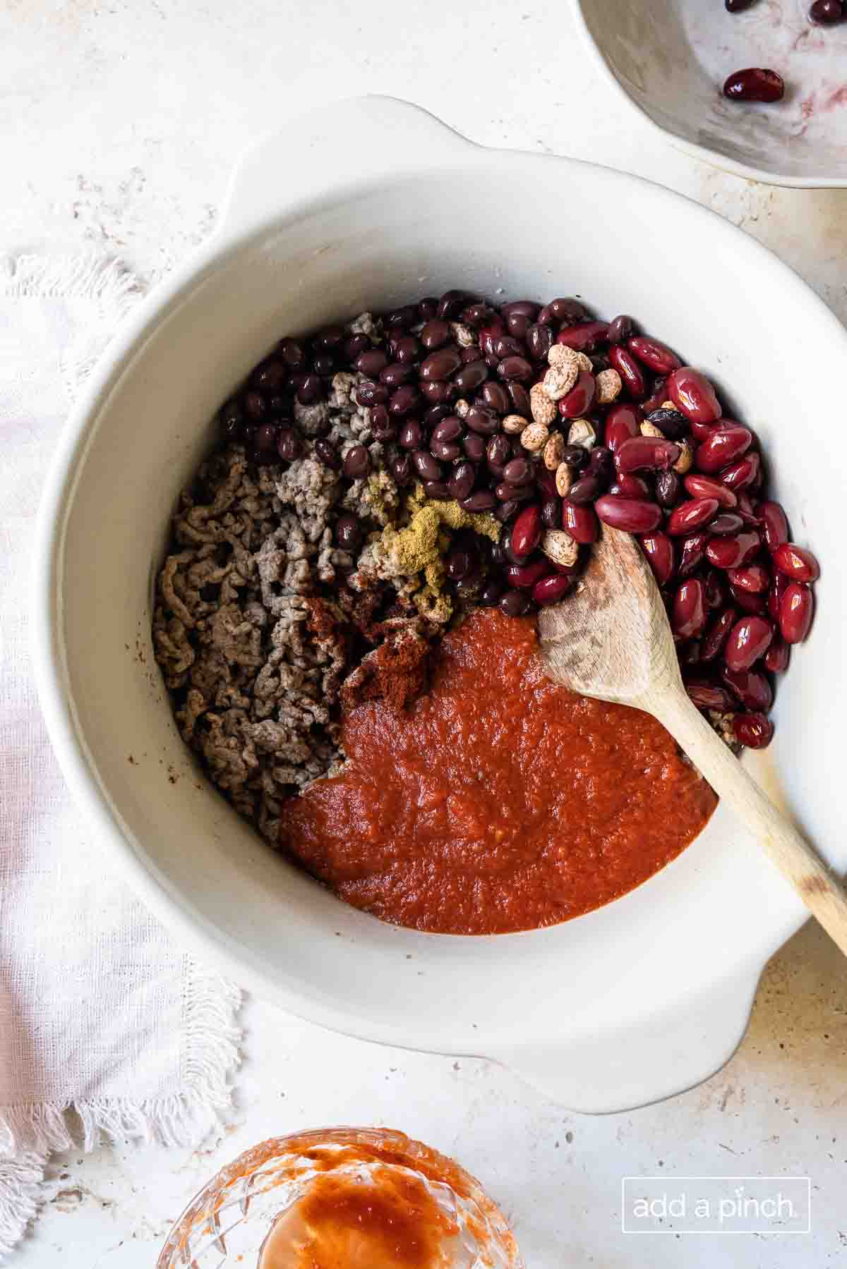 White Dutch oven with chili ingredients of beef, beans, tomatoes, and my three seasonings. 