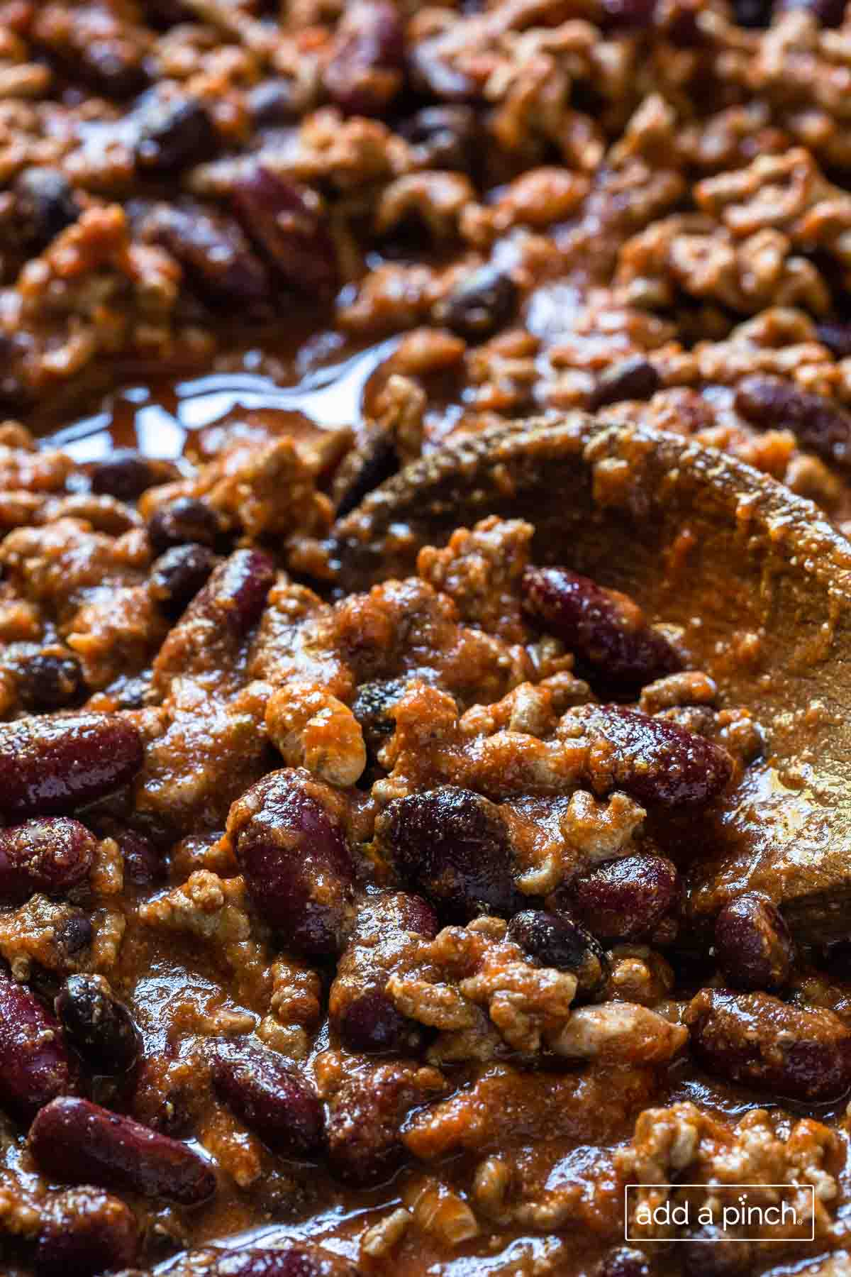 Chili with beef and beans with a wooden spoon in an up close photograph. 