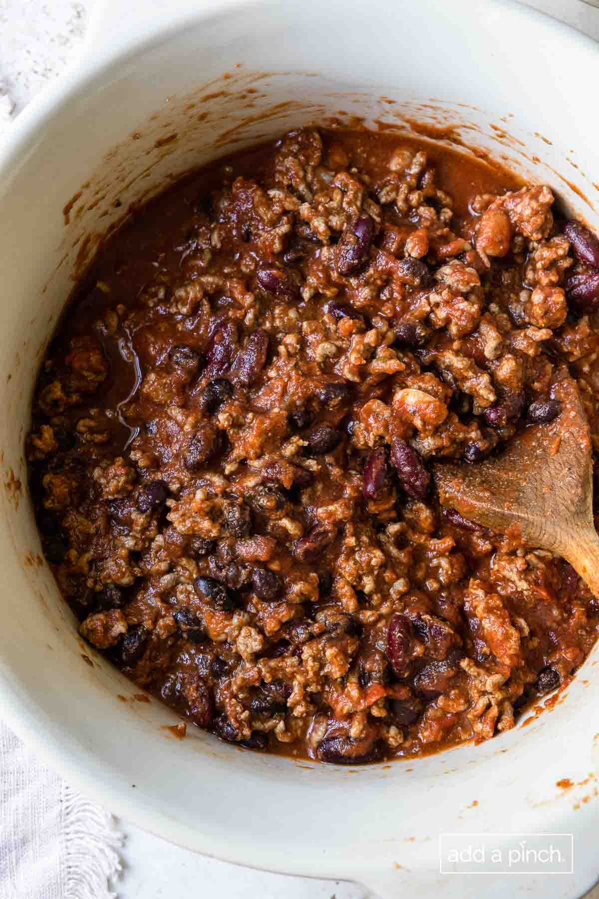 Chili simmering in a white Dutch oven and stirred with a wooden spoon. 