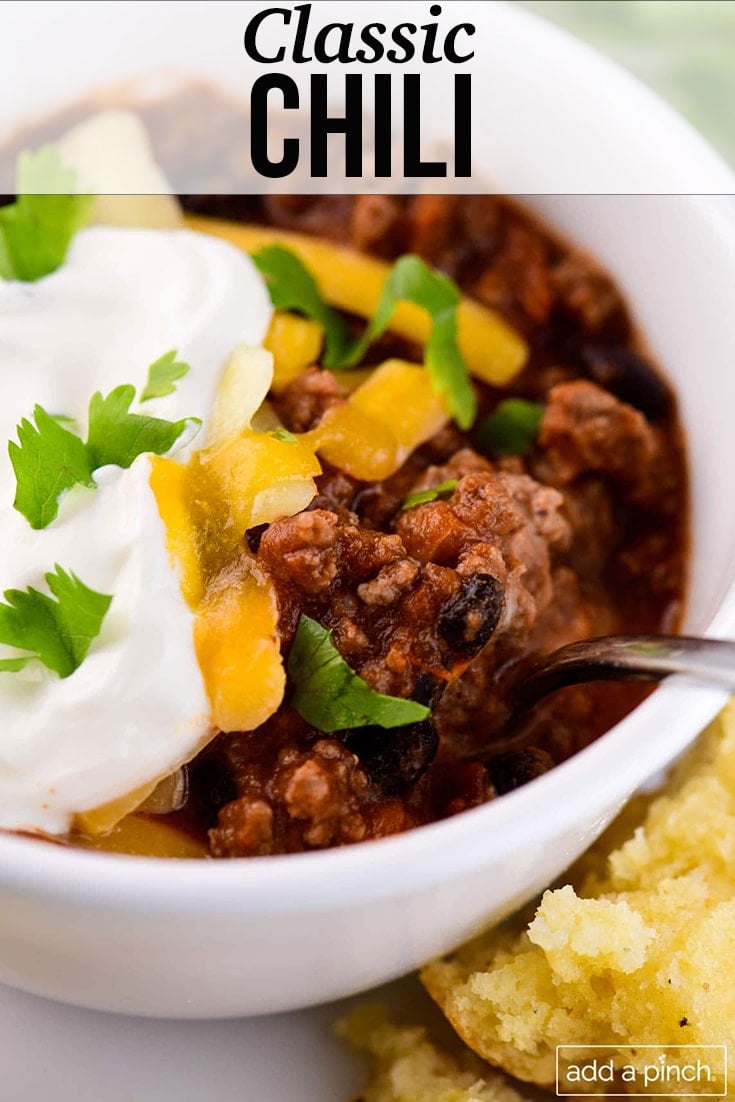 Bowl of chili topped with sour cream, cheese, and cilantro - with text - addapinch.com