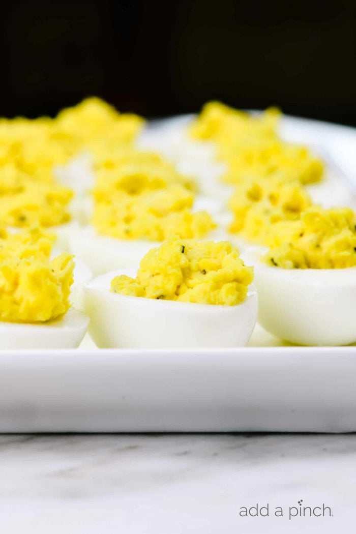 Photograph of hard boiled eggs that are stuffed on a white platter on a marble countertop.